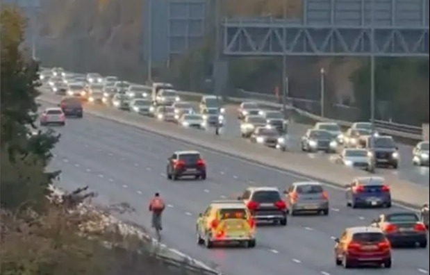 Moment idiot food delivery cyclist pedals along motorway in rush hour traffic